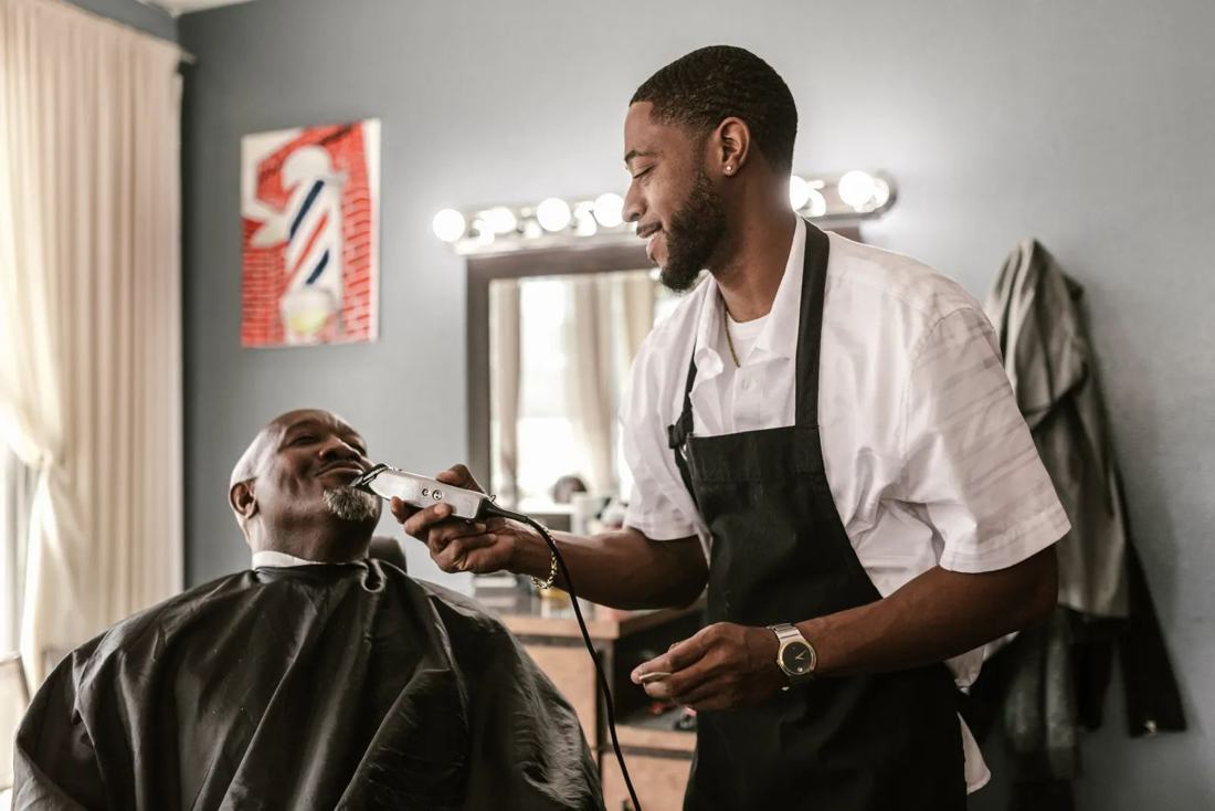 A barber trimming a client's beard with clippers
